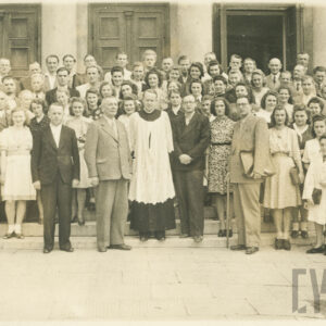 duża grupa kobiet i mężczyzn pozuje do fotografii na schodach przed wejściem do kościoła, w środku stoi ksiądz w sutannie i białej albie, z prawej chłopiec w białej koszuli i krótkich spodniach