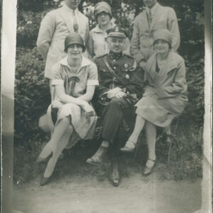 sześć osób pozuje do fotografii na tle drzew i krzewów, na pierwszym planie siedzi pośrodku mężczyzna w mundurze, po jego bokach dwie kobiety, za nimi pośrodku stoi kobieta, po bokach dwaj mężczyźni w jasnych garniturach