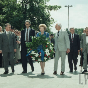 elegancka, starsza kobieta trzymająca w dłoniach wieniec idąca w towarzystwie starszych mężczyzn ubranych w garnitury