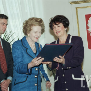 dwie elegancko ubrane kobiety, jedna przekazuje drugiej teczkę z dokumentami