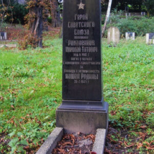 czarna tablica nagrobna z pozłacanym napisem cyrylicą w języku rosyjskim, wokół trawa, drzewa i inne nagrobki