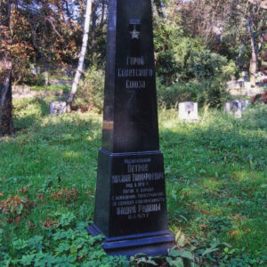 czarna tablica nagrobna z pozłacanym napisem cyrylicą w języku rosyjskim, wokół trawa, drzewa i inne nagrobki