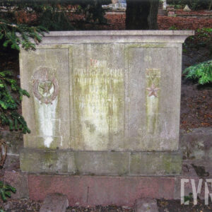 marmurowy, prostokątny nagrobek na cokole, z wyrytym cyrylicą napisem w języku rosyjskim, wokół trawa i drzewa