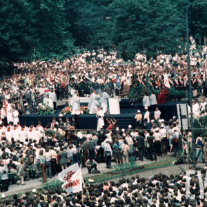 tłum osób zgromadzonych wokół prowizorycznego ołtarza, duża część z nich trzyma w rękach sztandary