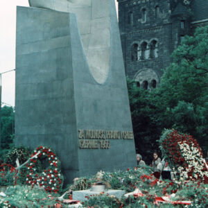 wieńce kwiatów leżące pod pomnikiem w formie monumentu z głową orła