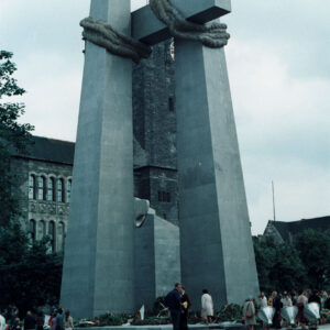 grupa osób stojących pod stalowym pomnikiem w formie dwóch krzyży i monumentu z głową orła
