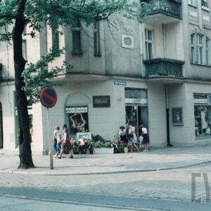 wieńce kwiatów pod tablicą pamiątkową zamontowaną na ścianie budynku z cegły przy skrzyżowaniu ulic