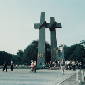 grupa osób stojących pod stalowym pomnikiem w formie dwóch krzyży i monumentu z głową orła