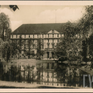 staw w parku otoczony okazałymi drzewami, w głębi duży budynek ze spadzistym dachem