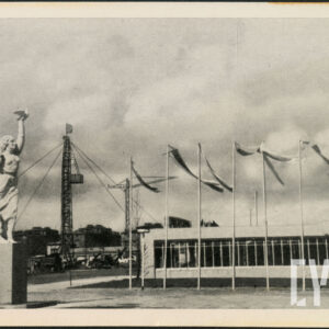 po lewej stronie rzeźba kobiety i mężczyzny na wysokim postumencie, w głębi niski pawilon, na tle którego powiewają flagi na wysokich masztach