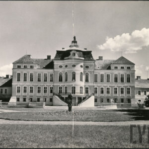 dwupiętrowy budynek stojący w ogrodzie ze spadzitym dachem z kilkoma szczytami, w elewacji rzędy wysokich okien, do budynlu prowadzą dwie pary schodów zbiegających się na pierwszym piętrze