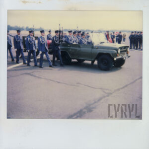 samochód, w którym siedzą żołnierze ciągnie lawetę wojskową na której leży trumna przykryta biało-czerwoną flagą, po obu stronach trumny idą żołnierze