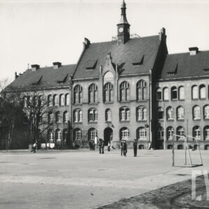 boisko do gry w piłkę nożną przed dużym, licowanym czerwoną cegłą, dwupiętrowym budynkiem, utrzymanym w stylu neogotyckim, z dachem uwieńczonym wieżyczką