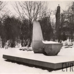 duży monument o nieregularnych kształtach umieszczony na kamiennej podstawie, wokół drzewa i groby
