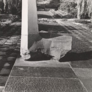 duży monument o nieregularnych kształtach umieszczony na kamiennej podstawie, wokół drzewa i groby