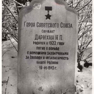 tablica nagrobna o nieregularnym kształcie, z wyrytym cyrylicą napisem w języku rosyjskim, wokół trawa i drzewa