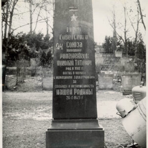 czarna tablica nagrobna z pozłacanym napisem cyrylicą w języku rosyjskim, wokół trawa, drzewa i inne nagrobki