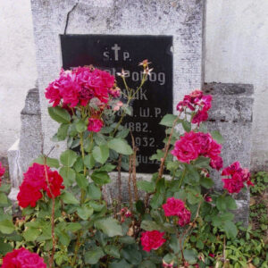 prostokątna tablica z napisami umiejscowiona na płycie nagrobnej; grób porośnięty różami