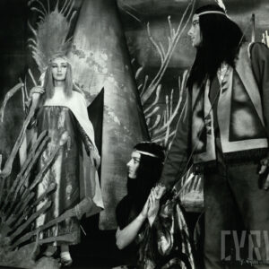 mężczyzna i dwie kobiety w strojach Indian, za nimi dekoracja z tipi