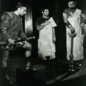 trzech stojących mężczyzn, dwóch z nich trzyma w rękach miecze