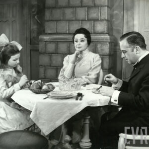 elegancko ubrani mężczyzna, kobieta i dziewczynka, spożywający posiłek przy stole w tle widoczny piec kaflowy