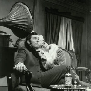 elegancko ubrani mężczyzna i kobieta siedzący na kanapie przy gramofonie, pijący koniak