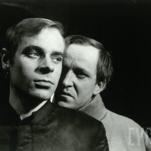 dwóch mężczyzn w średnim wieku; jeden stoi za drugim z nich