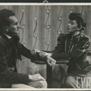 mężczyzna i kobieta siedzący przy stoliku; kobieta ściska dłońmi przedramię mężczyzny 