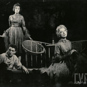 mężczyzna w średnim wieku siedzący między dwiema kobietami, jedna z nich stoi za nim, a druga siedzi obok