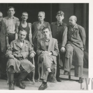 dwóch mężczyzn na krzesłach; za nimi sześciu na stojąco