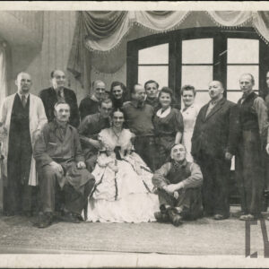 osiemnaście osób w różnych strojach; w tle szerokie okno z kotarą