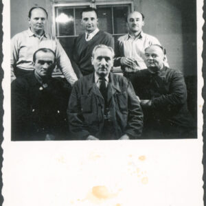 troje siedzących mężczyzn; z tyłu troje mężczyzn na stojąco; w tle okno