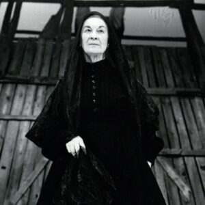 starsza kobieta w czarnej sukni stojąca na scenie