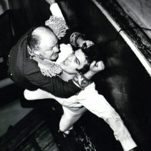 dwóch mężczyzn w kostiumach teatralnych, starszy z nich trzyma za koszulkę młodszego