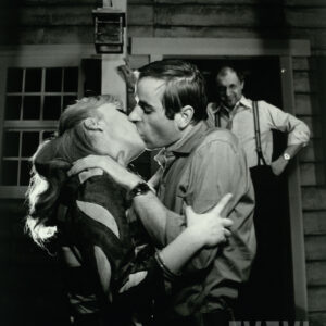 kobieta i mężczyzna w trakcie pocałunku, obserwowani przez mężczyznę stojącego za nimi