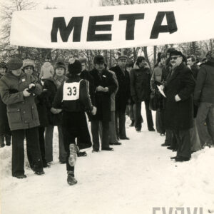 zimowa sceneria, grupa ludzi, przeważnie mężczyzn, w zimowych ubraniach stoi przy szrafie z napisem meta, do niej dobiega biegacz z numerkiem 33 na plecach