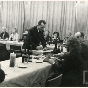 grupa kobiet i mężczyzn siedzi przy stołach, na nich napoje, szklanki, świeca, jeden z mężczyzn stoi