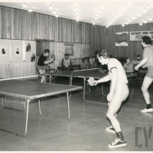 pośrodku sali ustawione dwa stoły do tenisa stołowego, przy nich gracze