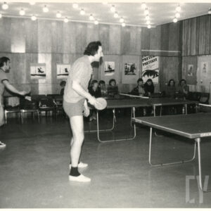 pośrodku sali dwa stoły do tenisa stołowego, przy nich gracze