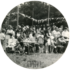 duża grupa dzieci w towarzystwie dorosłych na polanie, część siedzi na drewnianych ławkach