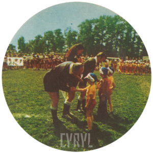 trójka małych dzieci podaje rękę dwóm mężczyznom i kobiecie, w głębi duże grupy dzieci