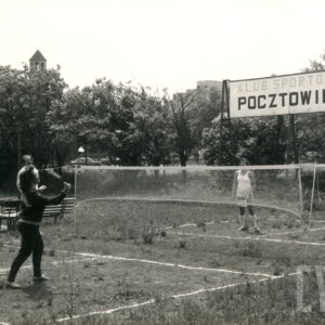 dwaj zawodnicy grają w badmintona na małym, zaniedbanym korcie, na środku rozciągnięta siatka