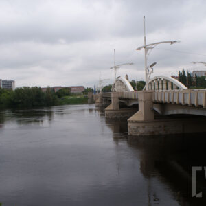 most łączący dwa brzegi, pod nim rzeka o wyraźnie podniesionym stanie; w głębi zarysy budynków