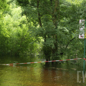 tereny zielone zalane wodą; widoczne zalane drzewa oraz rozwieszona pomiędzy nimi taśma zakazująca wstępu na ten teren