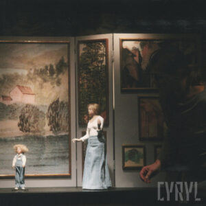 lalka chłopca i kobiety na tle obrazów przedstawiających krajobrazy i drzewa, z prawej aktorka spoglądająca na lalki