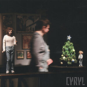 lalki mężczyzny i chłopca, między nimi aktorka, w głębi powieszone obrazy