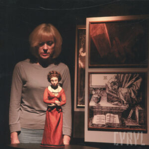 na pierwszym planie lalka kobiety, za nią stoi aktorka, z prawej fragment scenografii - dwa obrazy