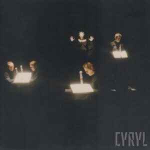 czwórka ludzi siedzi w ciemności, światło skierowane tylko na nich,, z tego dwie osoby siedzą same a dwie w parze, wszyscy trzymają w rękach płaski przedmiot jakby blachę, która odbija skierowane na nich światło, w głębi oświetlona kukła