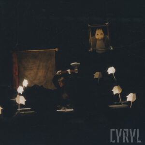 dość ciemna scena spektaklu, oświetlone niektóre elementy scenografii, pośrodku mężczyzna z uniesioną nad głową siekierą