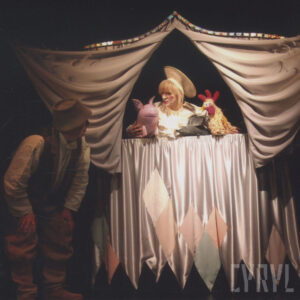 teatrzyk lalkowy ułożony z tkanin, na górze aktorka z trzema lalkami: świnki, myszki i kogucika, z lewej aktor w kostiumie 